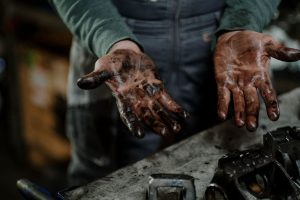 mainile unui mecanic auto manjite cu vaselina cu o pisa de motor pe un banc de lucru